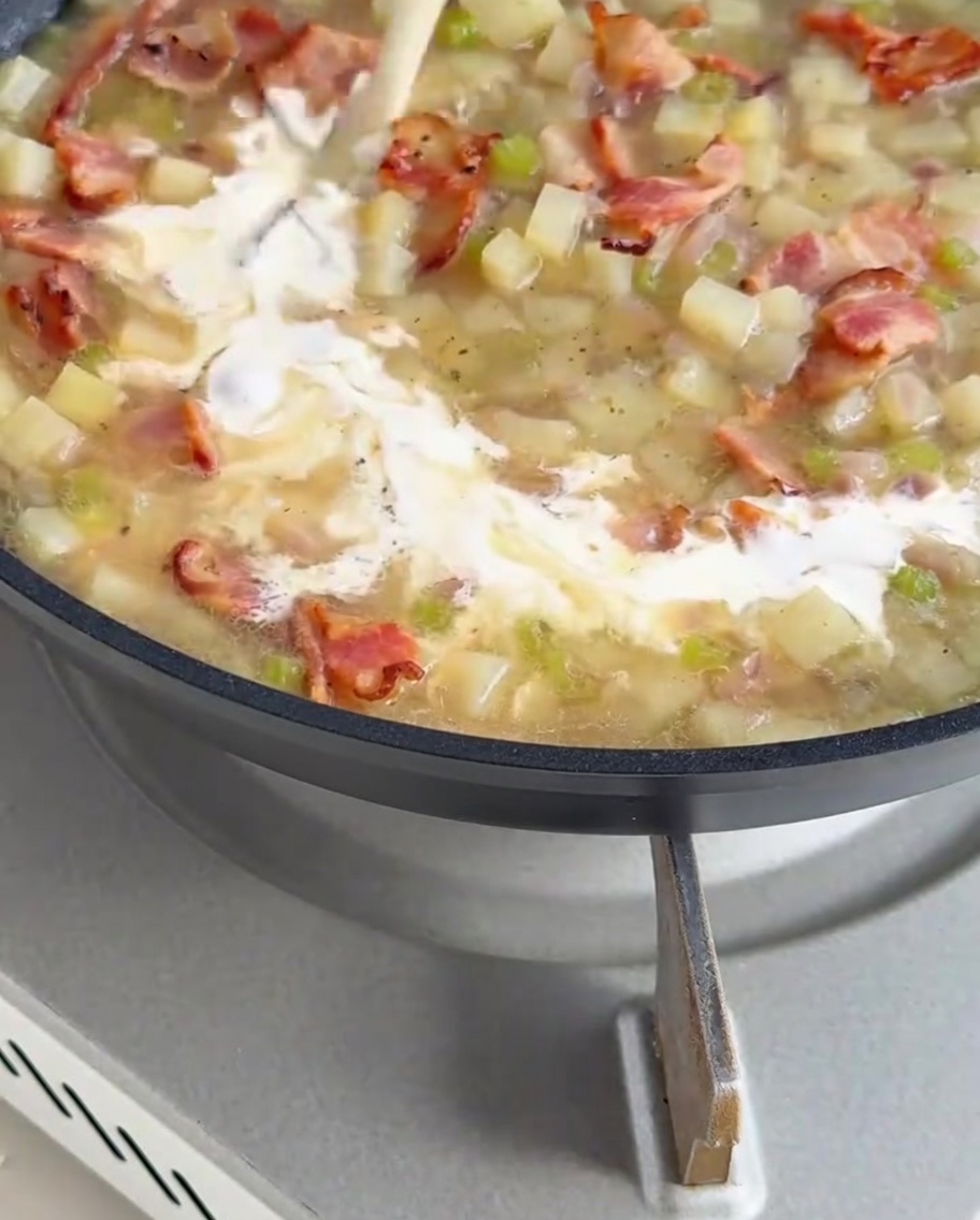 Thick, creamy white sauce being poured into the pan of simmering clam chowder base.