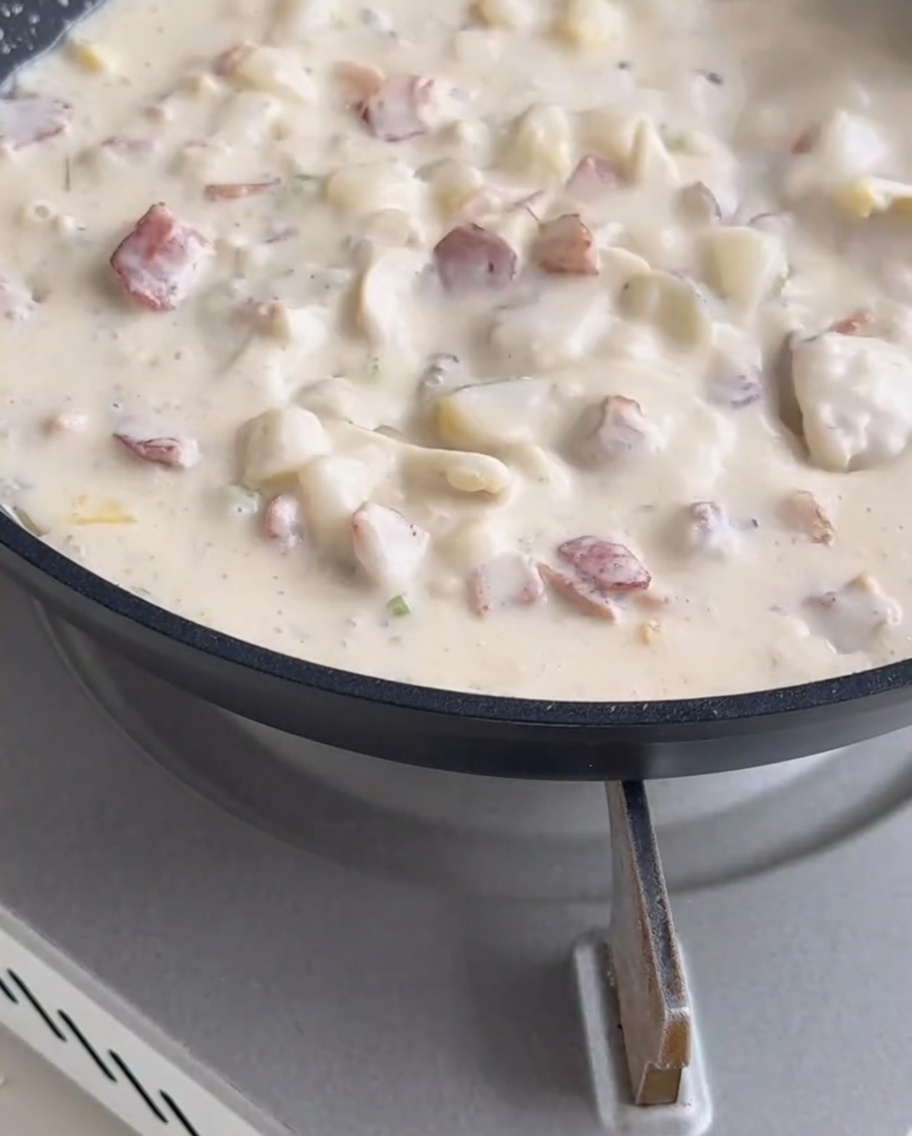 Clam meat being stirred into the creamy, bubbling soup in the pan.