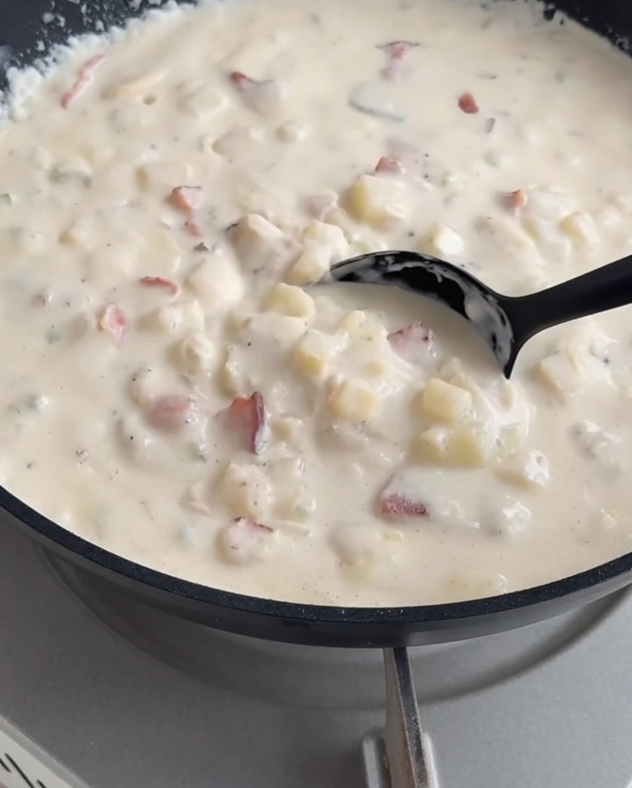 Creamy clam chowder being ladled from a pot into a prepared crusty bread bowl.