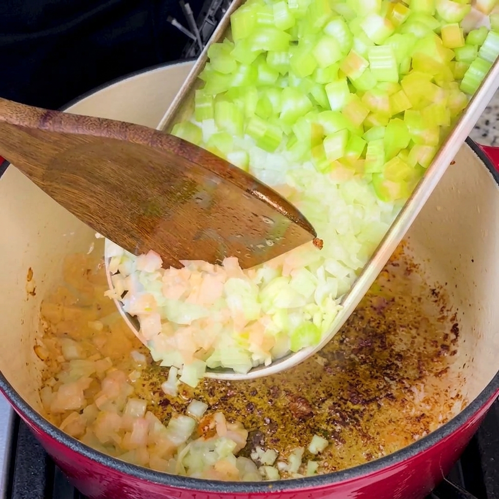 The mix of diced vegetables sautéing in a red Dutch oven coated with rendered bacon fat.