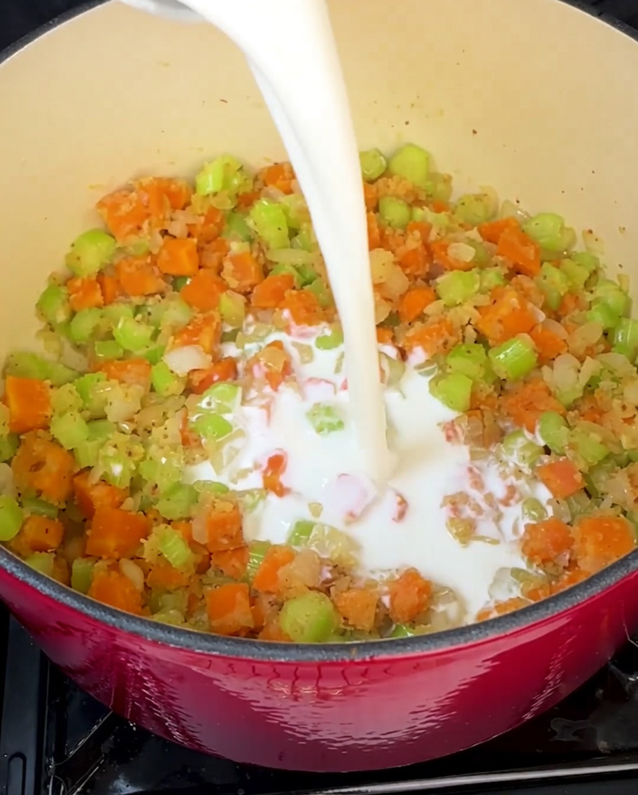 Cream and milk being poured into the pot to create the rich, smooth soup base.
