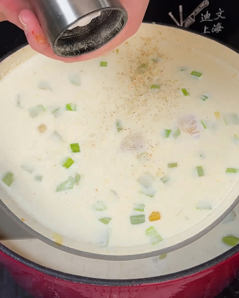 Bay leaf and fresh thyme being added to a simmering pot of creamy clam chowder.