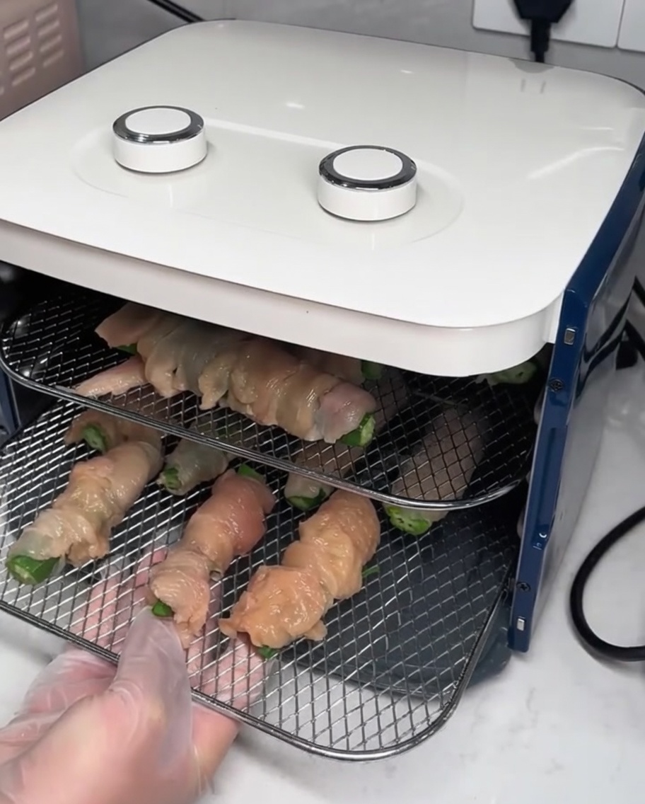 Metal drying racks with assembled chicken wraps being slid into a food dehydrator.