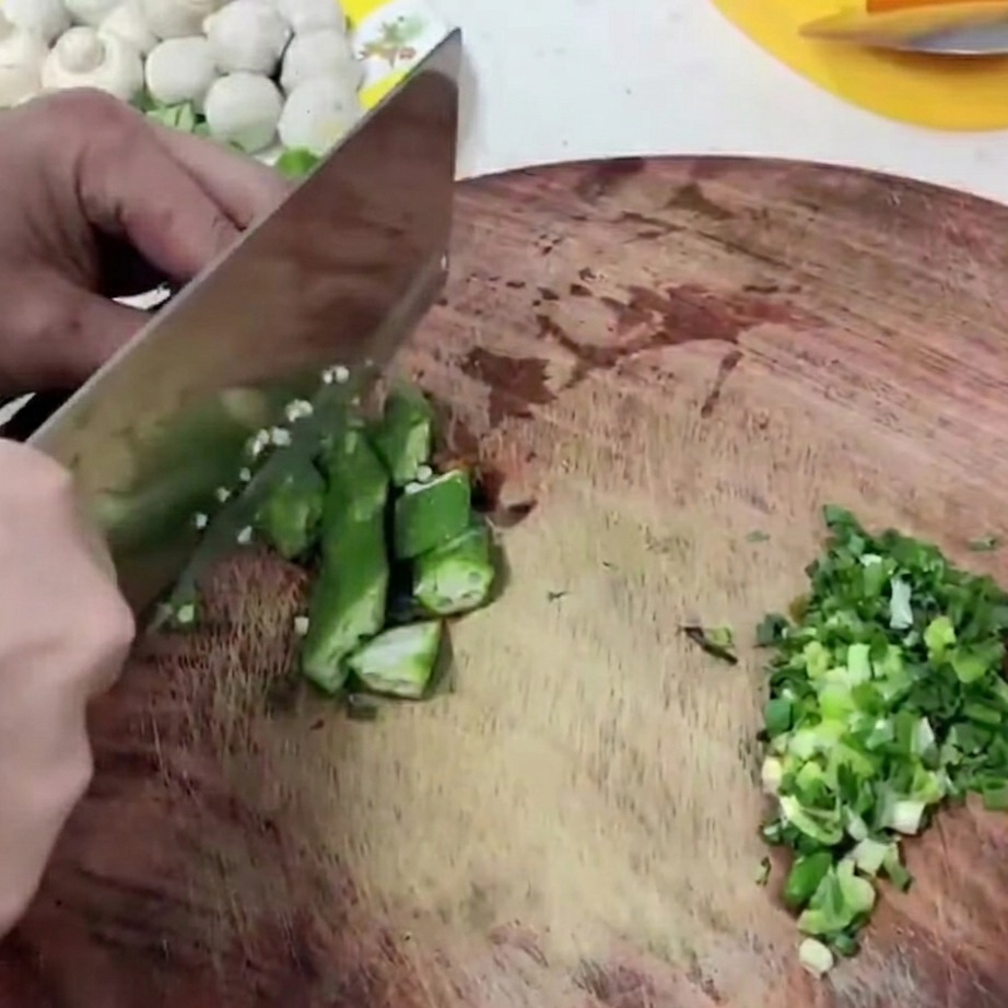 Fresh green okra segments being cut on a wooden cutting board.