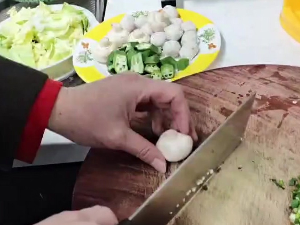White button mushrooms being diced into small pieces on a wooden surface.