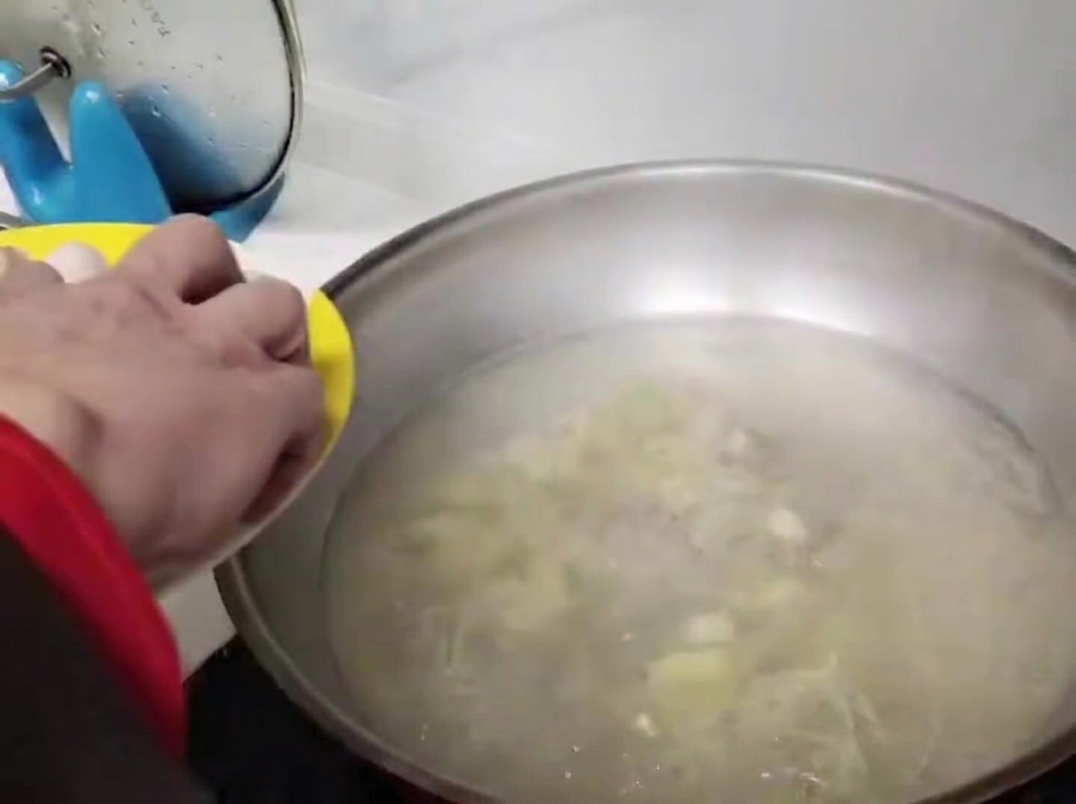 Round meatballs being carefully placed into the bubbling water in a stainless steel wok.