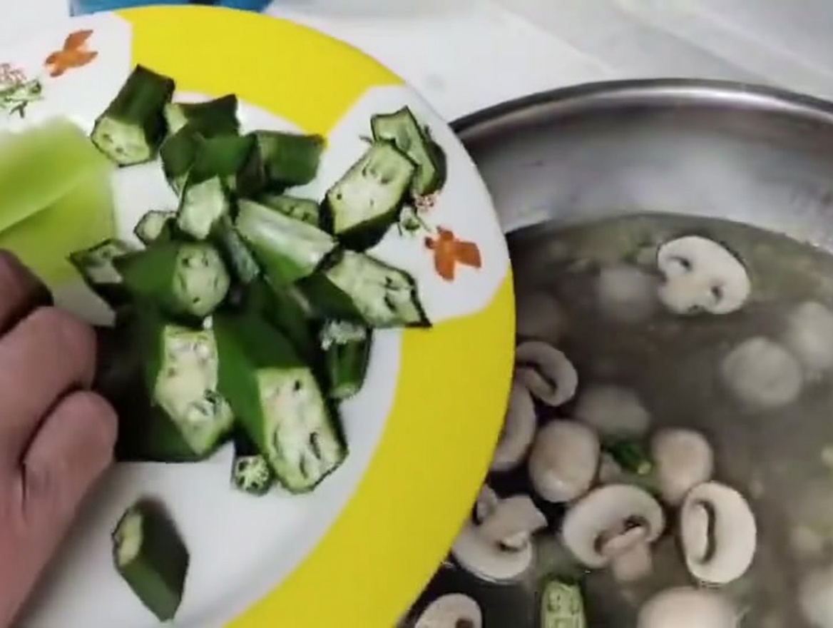 Freshly sliced mushrooms and okra segments being dropped into the simmering meatball soup.