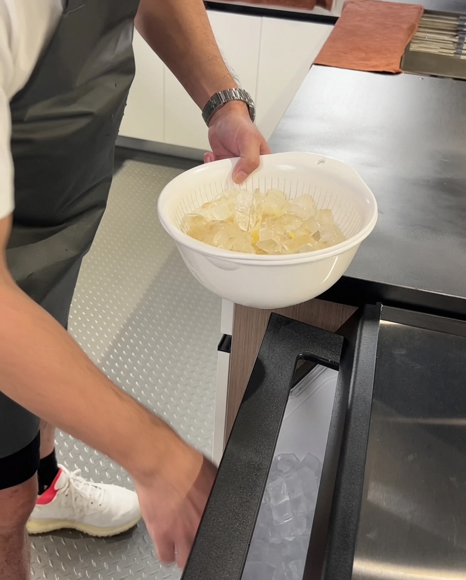 Cooked pasta being transferred into a bowl filled with ice cubes.