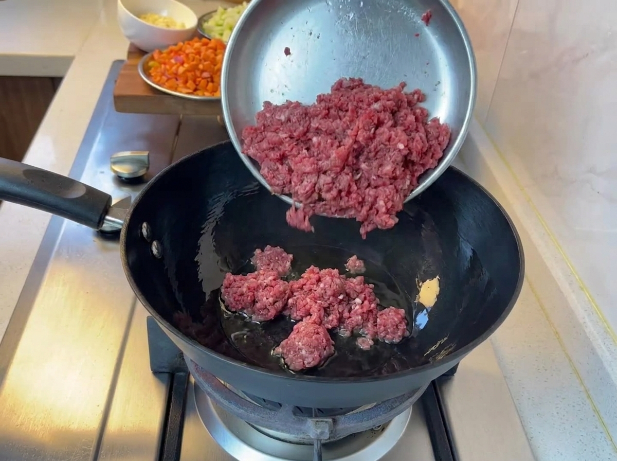 Minced beef cooking in a black pan over a gas stove.