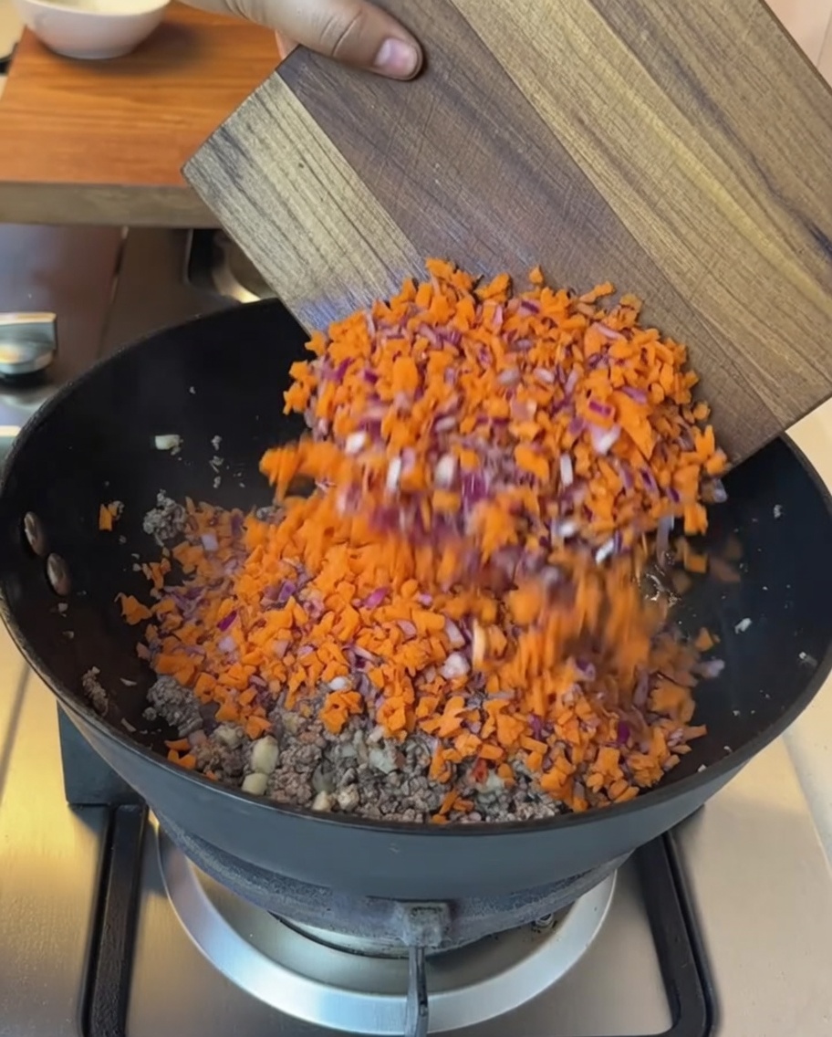 Minced vegetables and diced tomatoes being added to the pan with cooked beef.