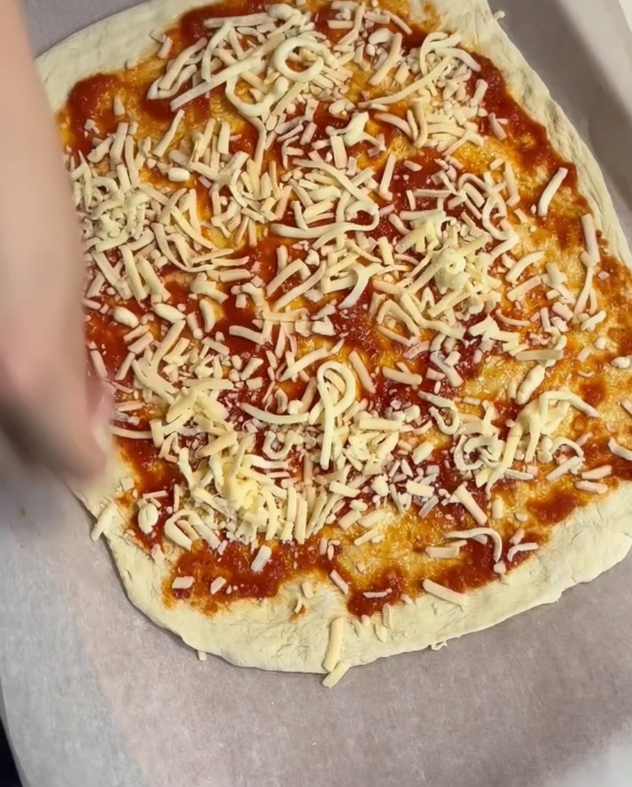 A layer of shredded cheese being sprinkled over the tomato sauce base.