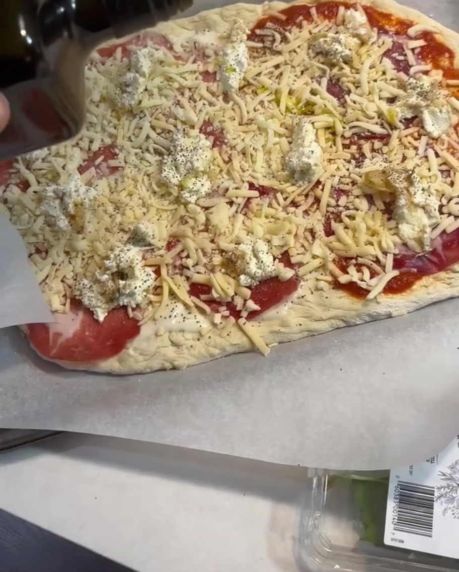 A light drizzle of olive oil being applied over the assembled pizza toppings.