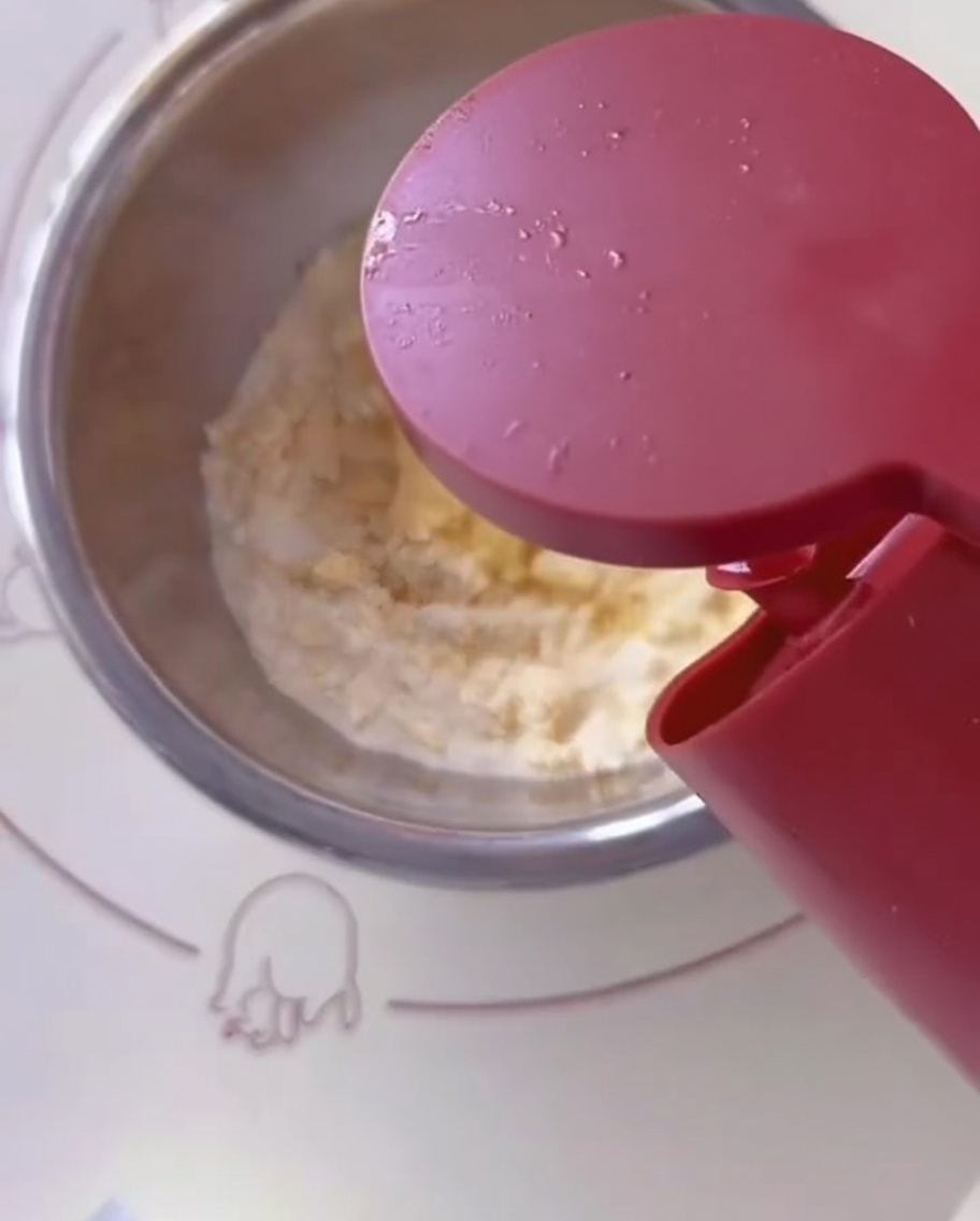 Cooking oil being poured from a container into the mixing bowl with flour and egg.