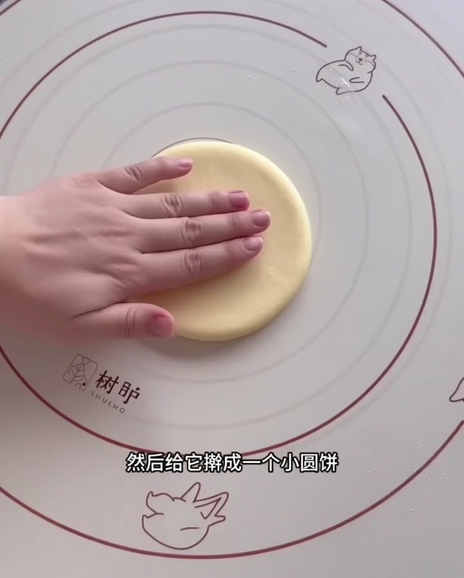 A portion of dough being flattened into a circle using a wooden rolling pin on a silicone mat.