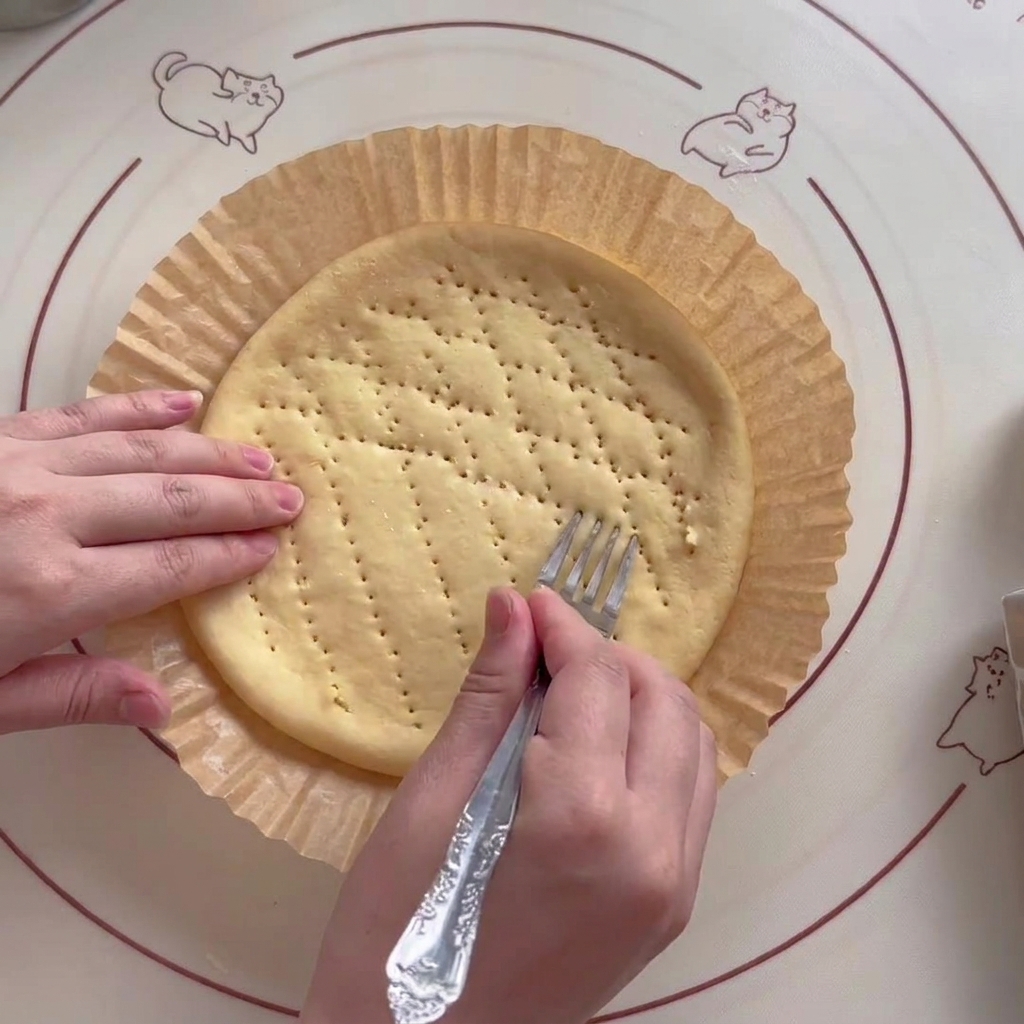 A metal fork being used to pierce the dough base to prevent it from rising too much during baking.