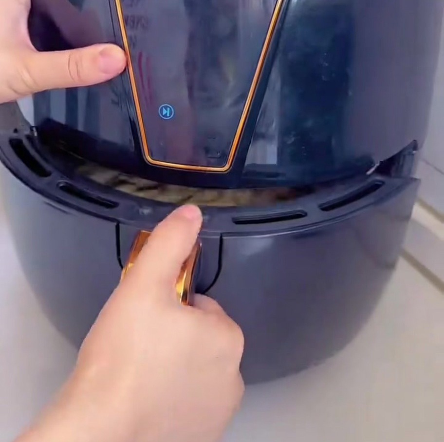 A hands-on view of sliding the drawer of a black air fryer, containing the prepared pizza on parchment paper.