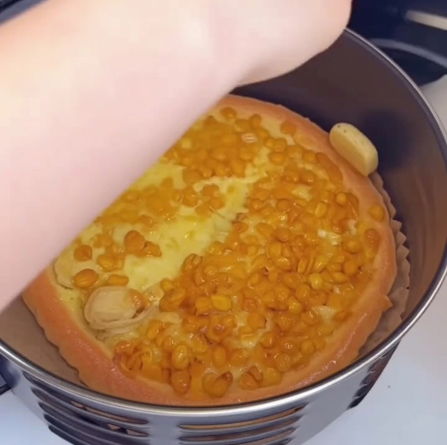 A hand using a small brush to apply oil to the golden-brown edge of a partially baked pizza inside the air fryer.
