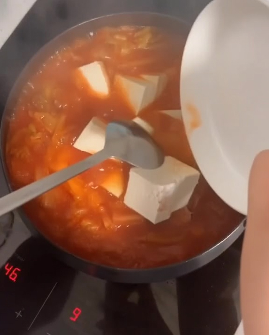 Soft tofu cubes being added to the bubbling red kimchi stew.