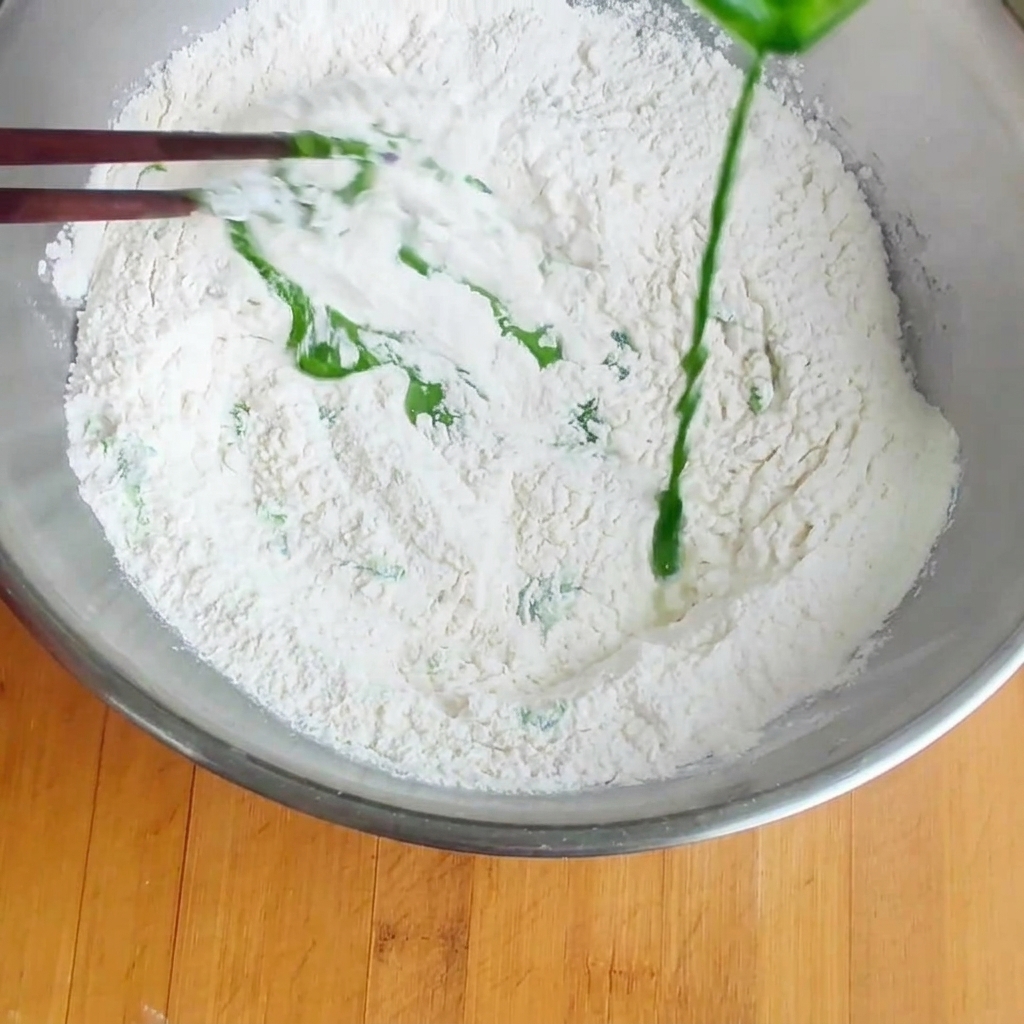 Spinach juice being poured into a large bowl of flour, ready to be mixed.