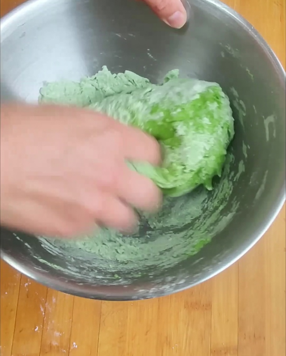 Hand mixing the spinach-infused flour to form a consistent green dough.