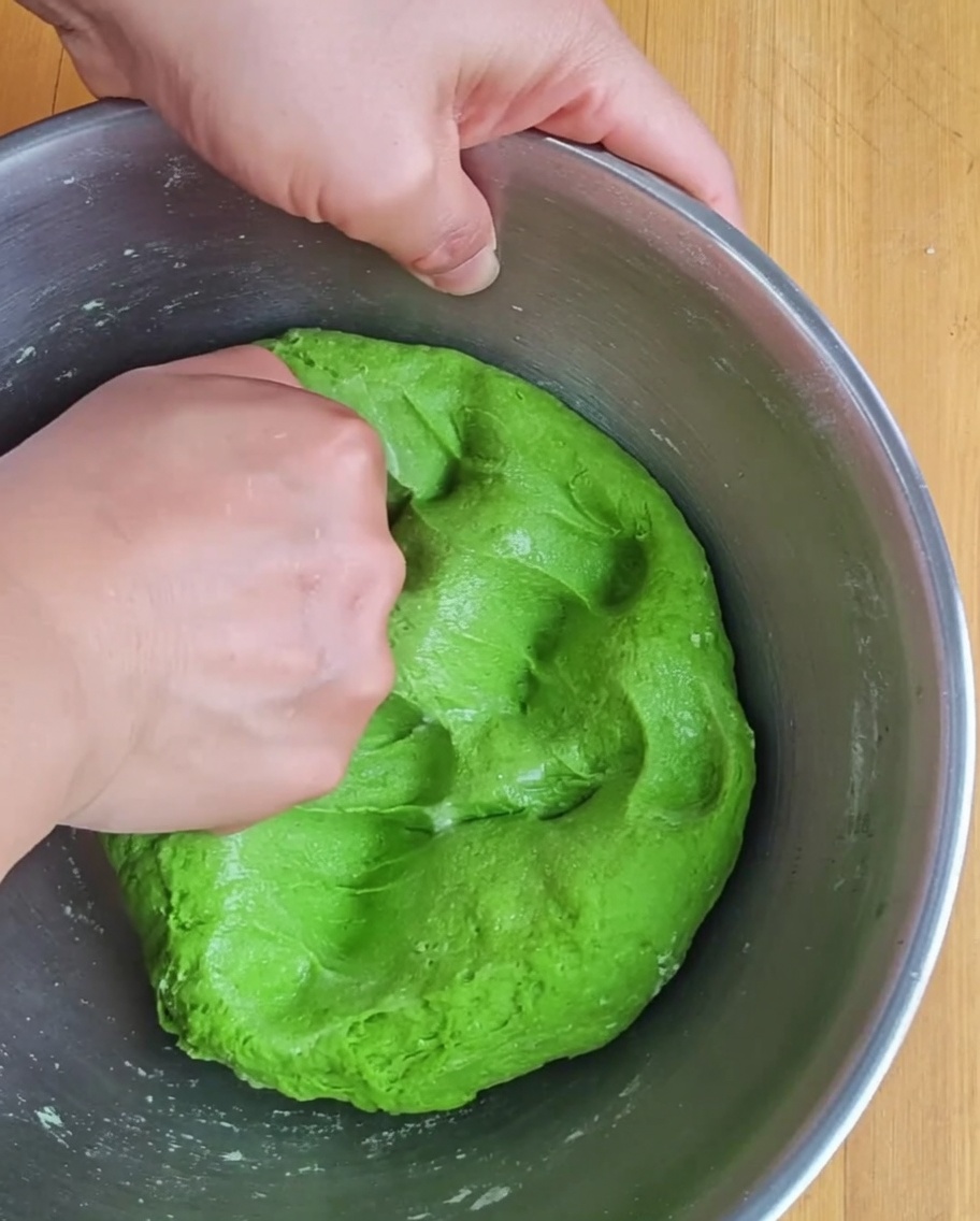 Punching the green dough in a metal bowl to begin the gluten development.