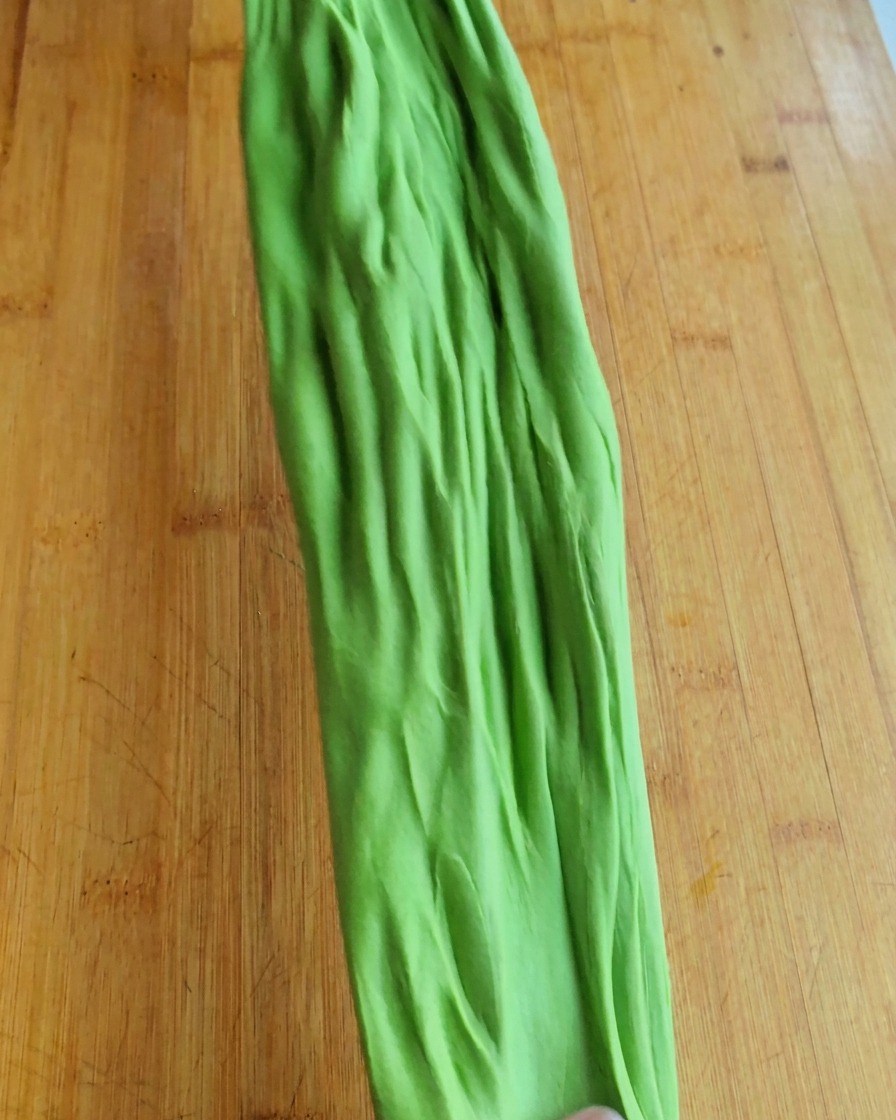 A piece of green dough being stretched to show its elasticity and gluten development.
