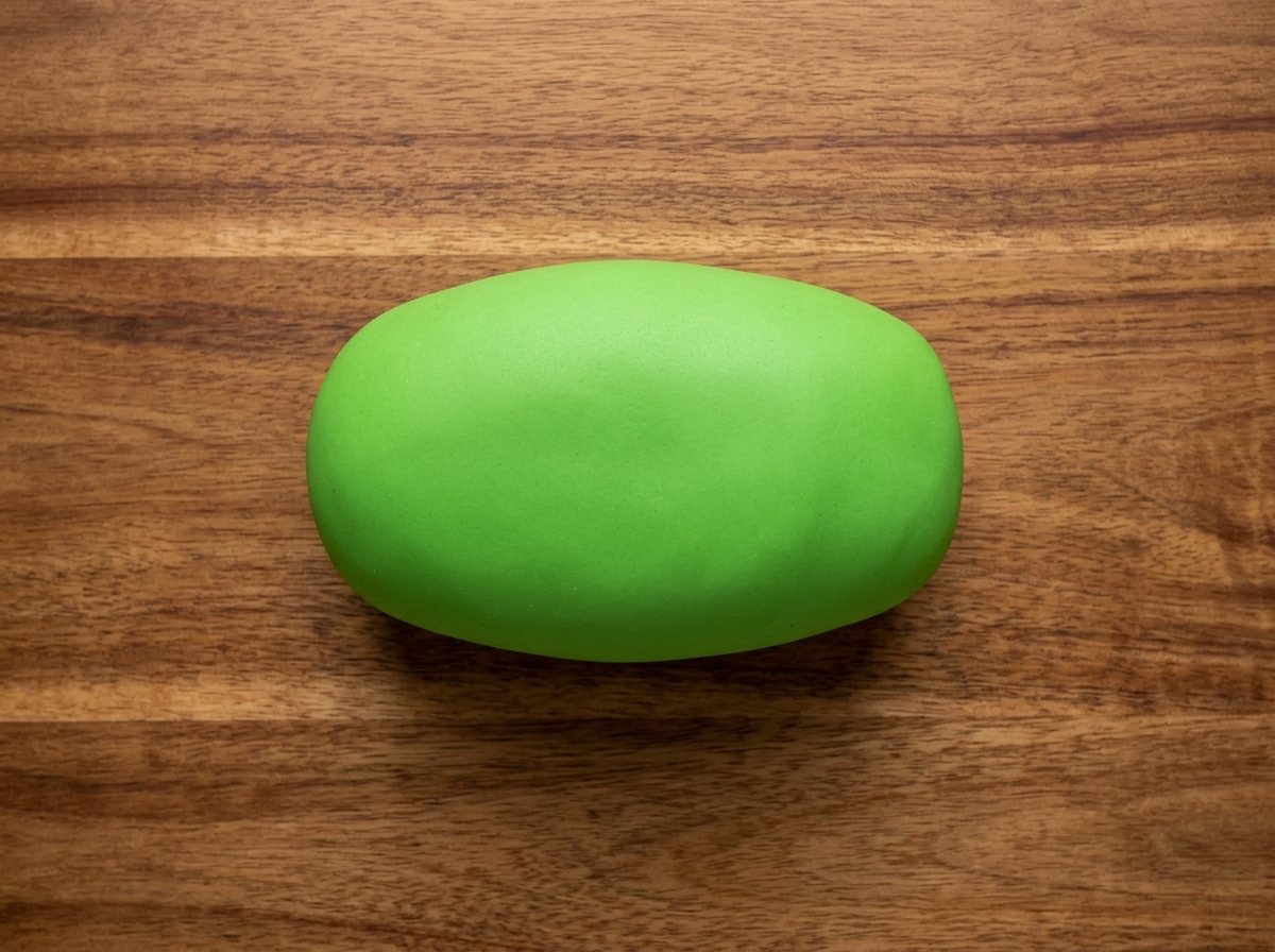 A knife cutting a green dough ball into several even portions on a wooden board.