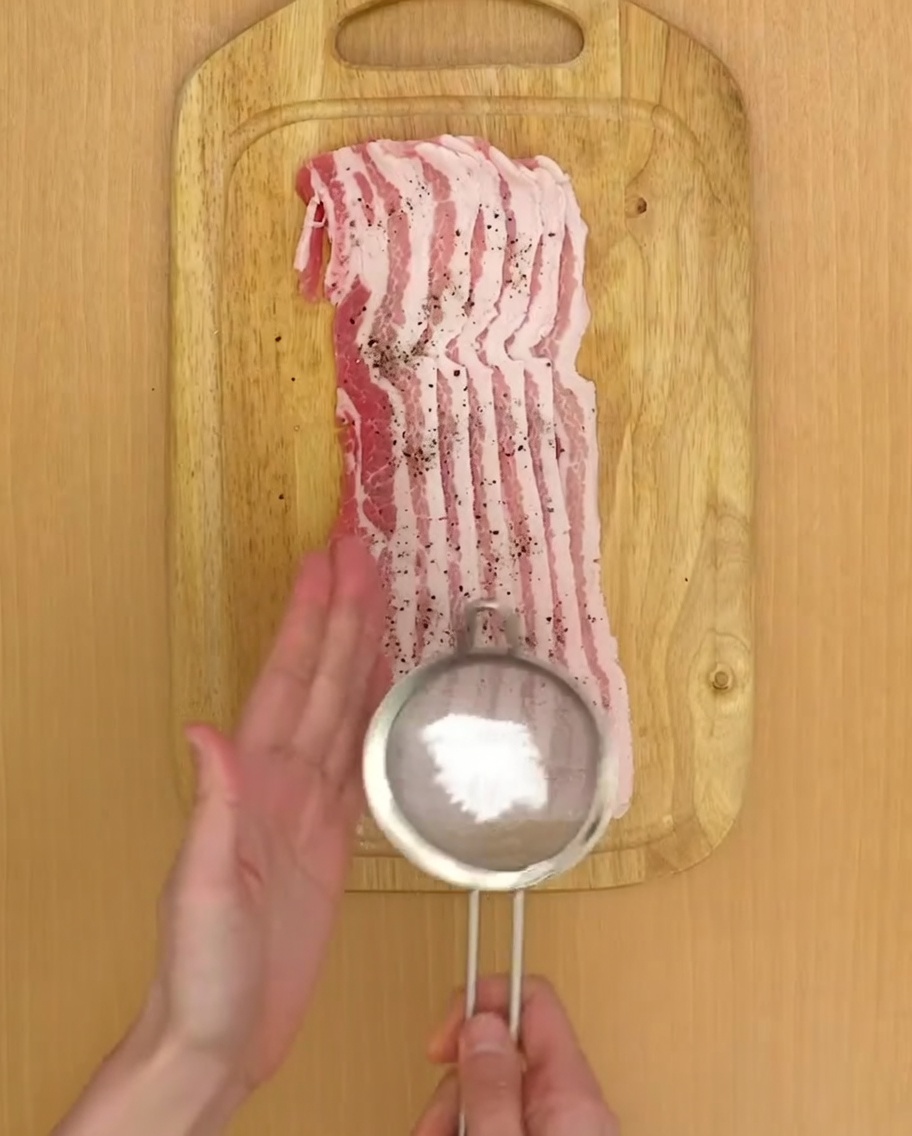Starch being sifted over seasoned pork belly stacks on a cutting board.