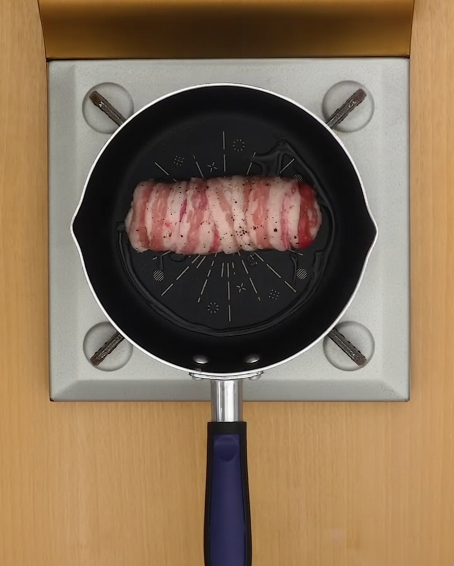 A rolled pork belly cylinder browning in a pan with a small amount of oil.
