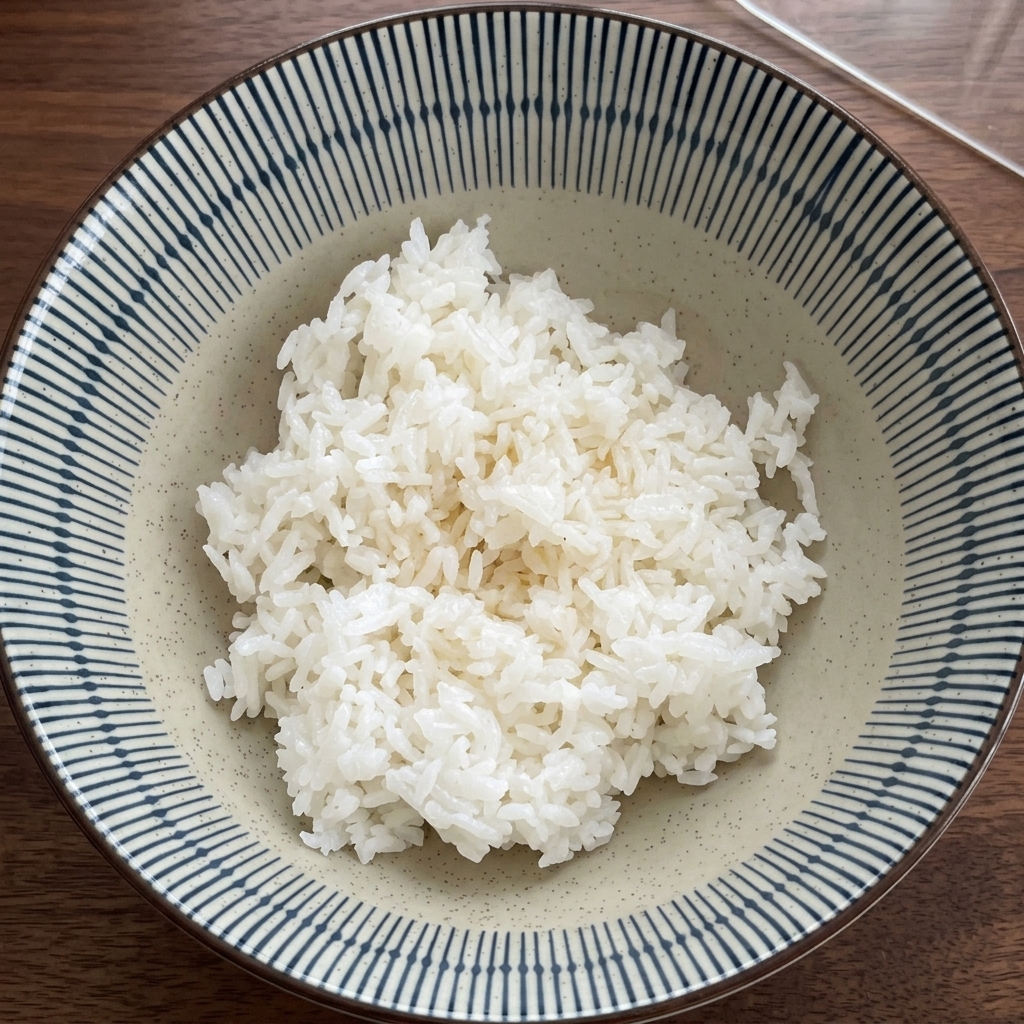 A bowl of white rice being mixed with dark shredded seaweed by a hand wearing a plastic glove.