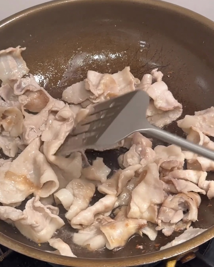 Onion, scallions, and chili slices being tossed into a pan with pork belly pieces.