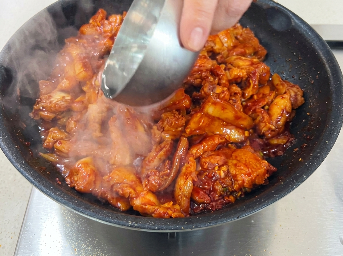 Marinated pork belly simmering in a covered pan with a small amount of added water.