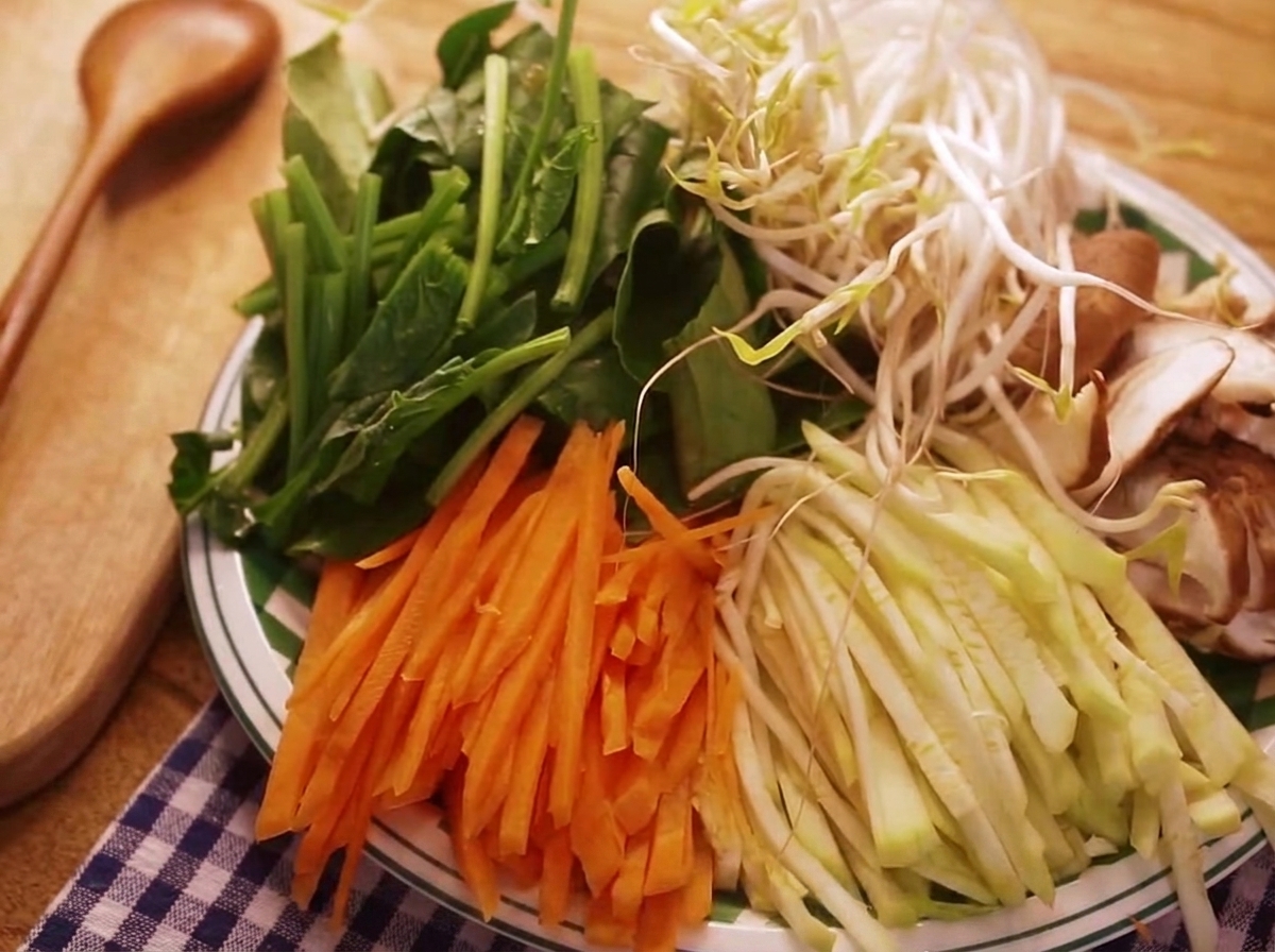 A colorful array of julienned vegetables including carrots, zucchini, and spinach, prepared for the bibimbap.