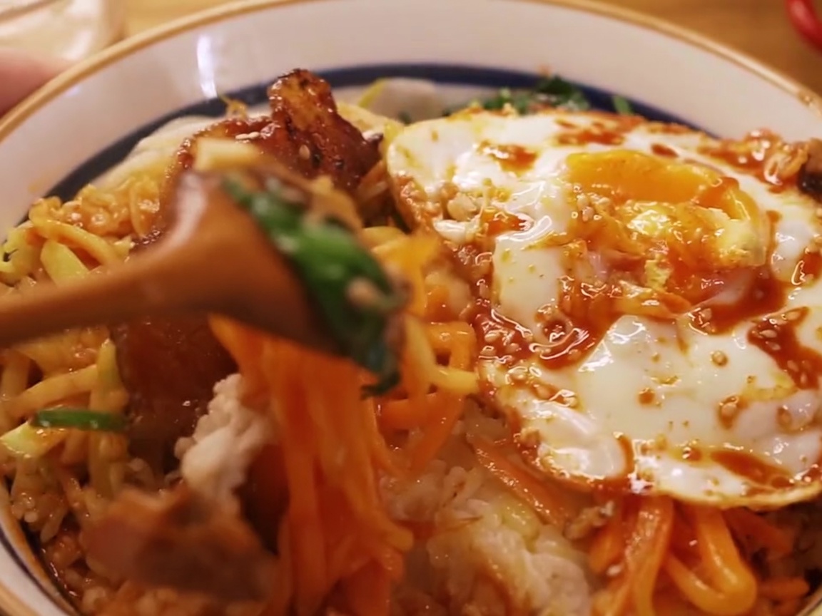 Close-up view of a wooden spoon mixing all the bibimbap ingredients together in the bowl.