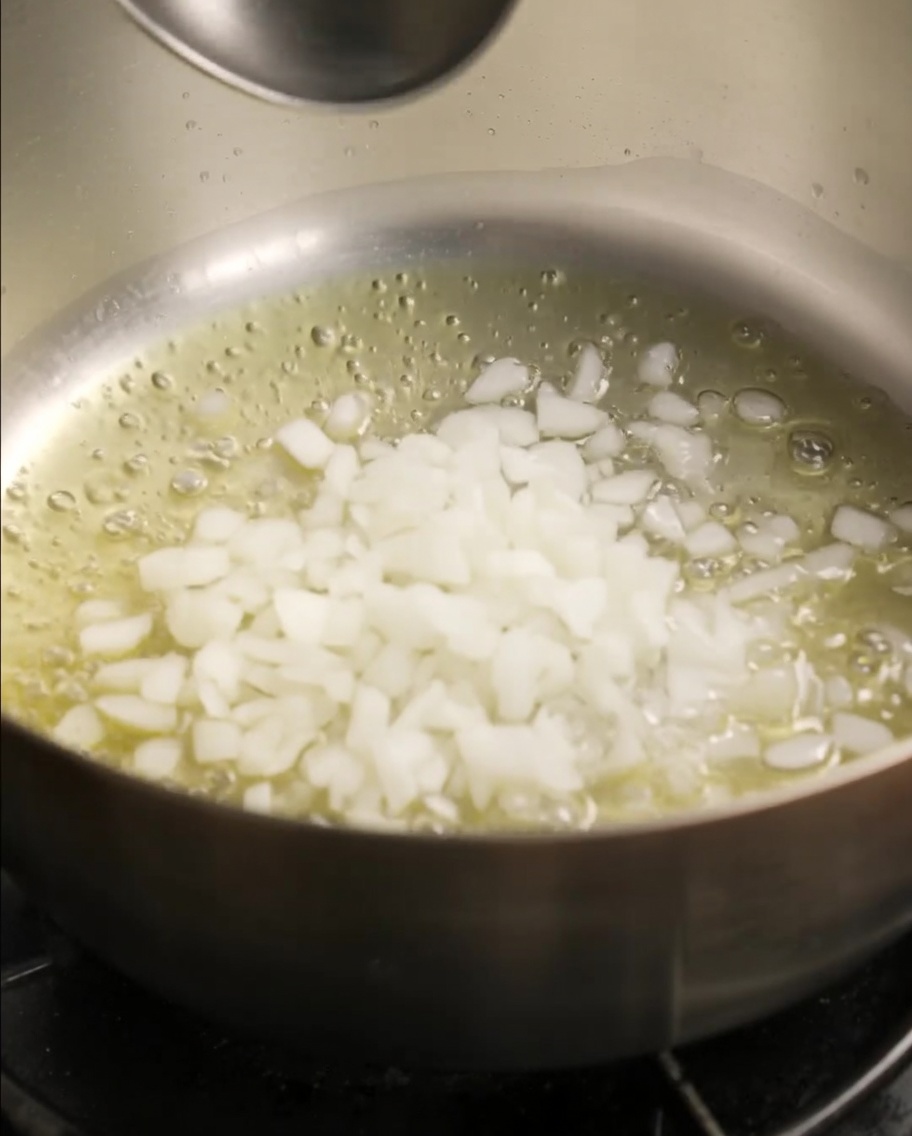 Finely chopped white onions and sliced mushrooms frying in a pan with melted butter.