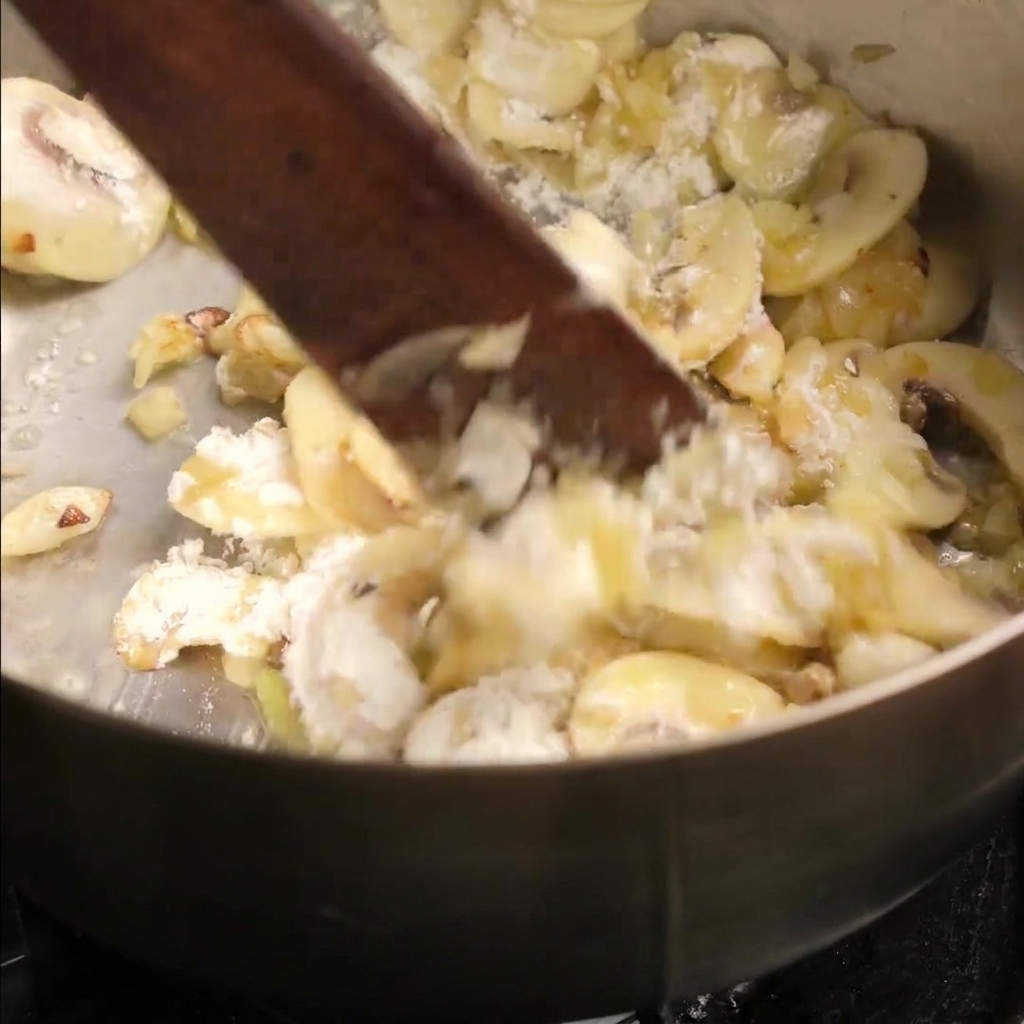 Beef broth being poured into the pan over the sautéed mushroom and flour mixture.