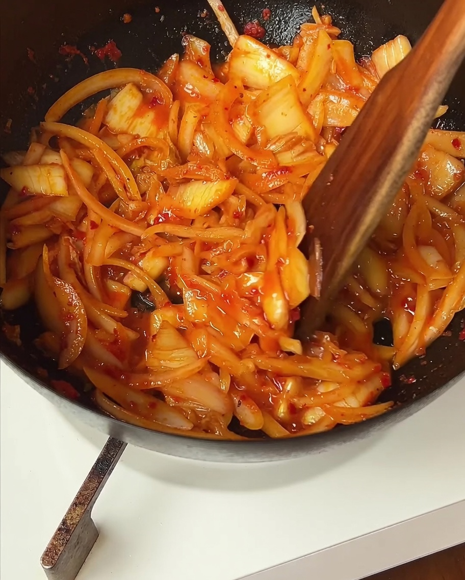 Browned beef being stirred back into the pan with the sautéed kimchi and onions.