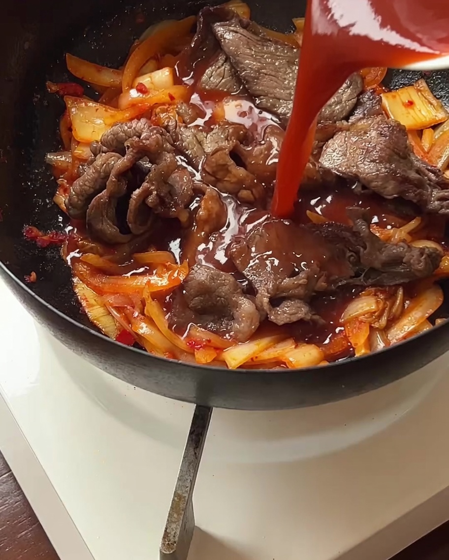 Sauce being poured over the beef and kimchi mixture in the pan, coating all ingredients.