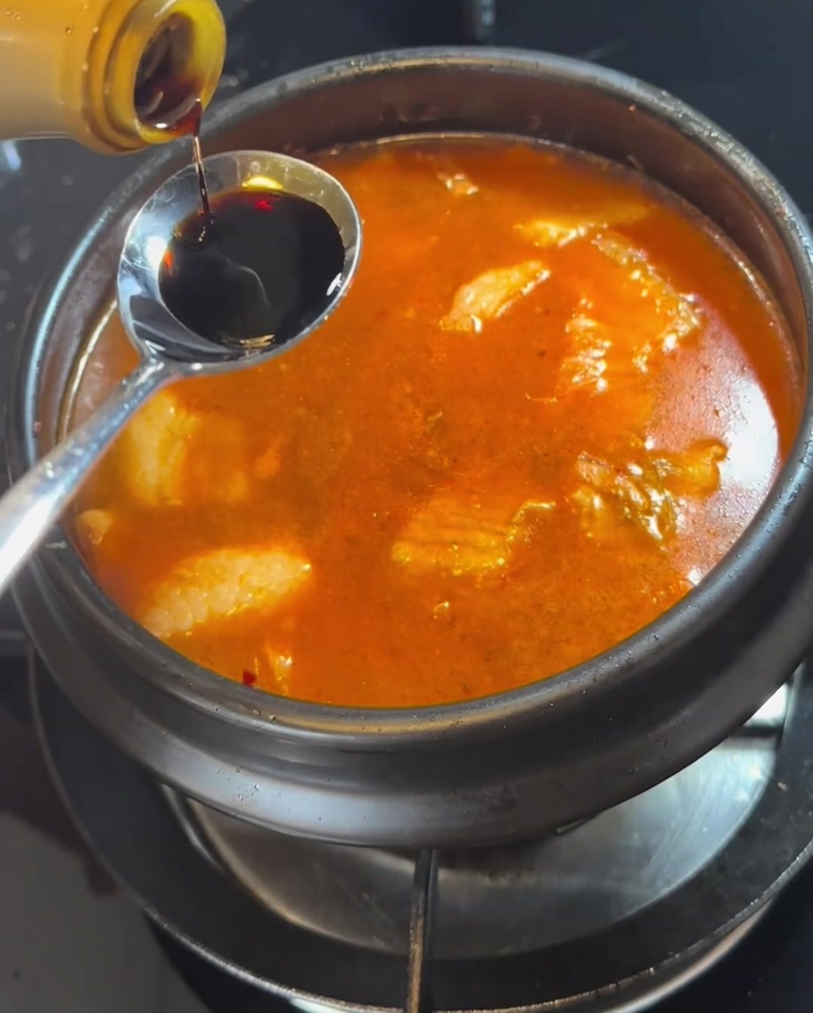 A spoonful of soy sauce being added to the bubbling stew.