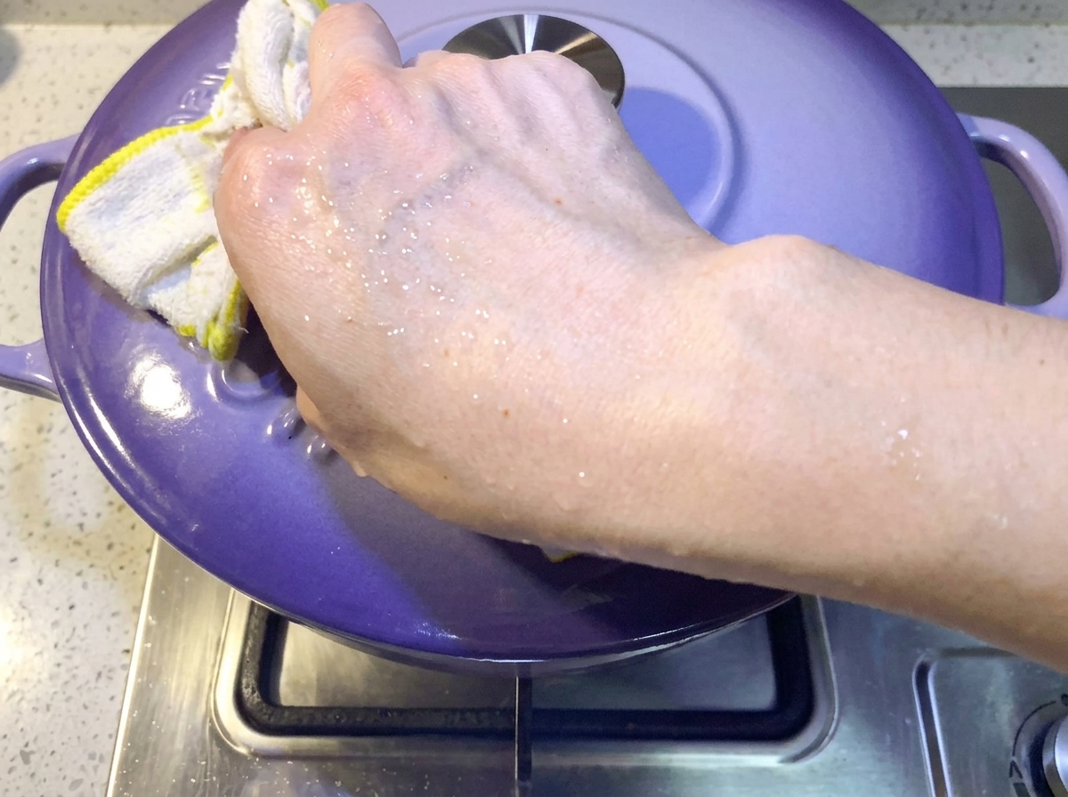 Hand placing a purple lid onto the pot to cover the kimchi pork rib stew.