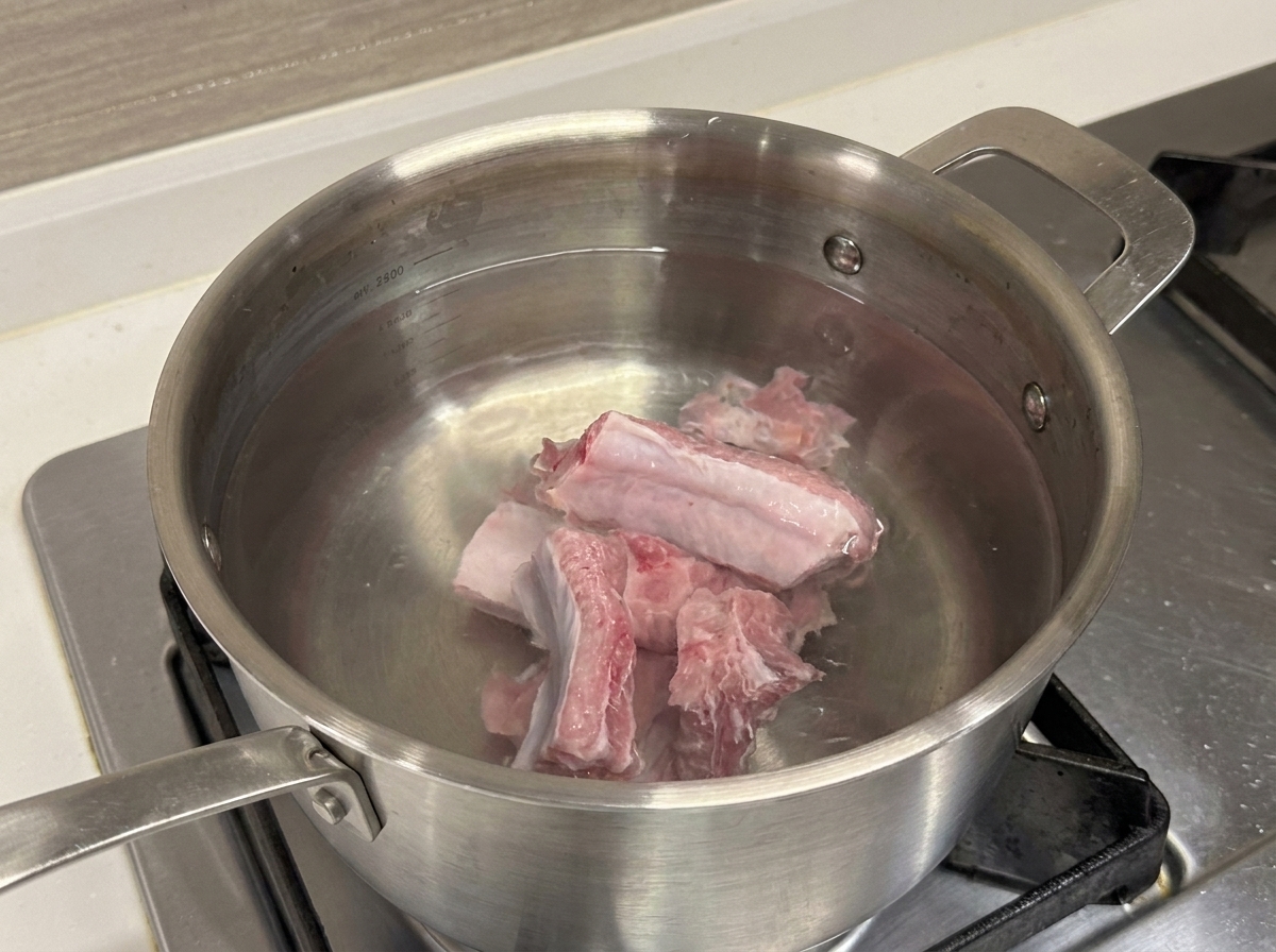 Raw pork ribs sitting in a stainless steel pot filled with cold water.