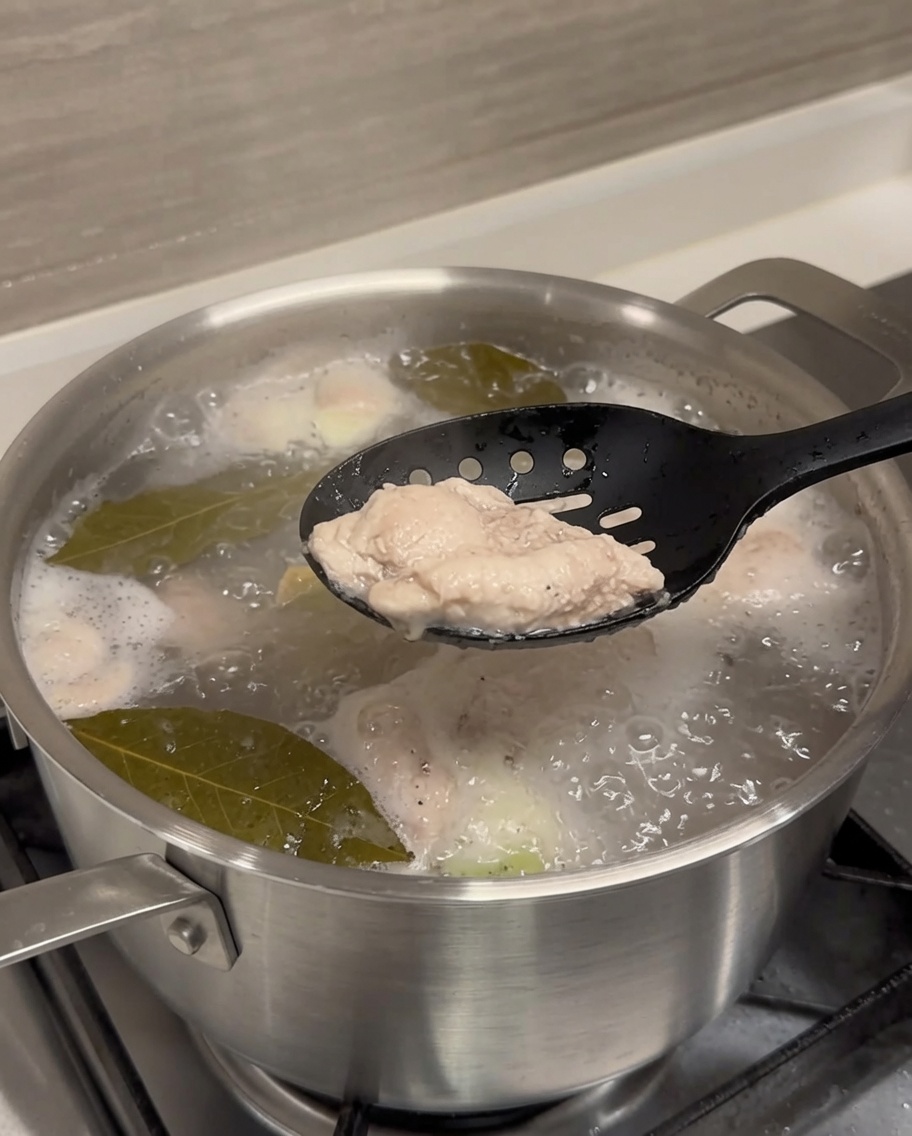 A blanched pork rib being lifted from boiling water with black tongs.