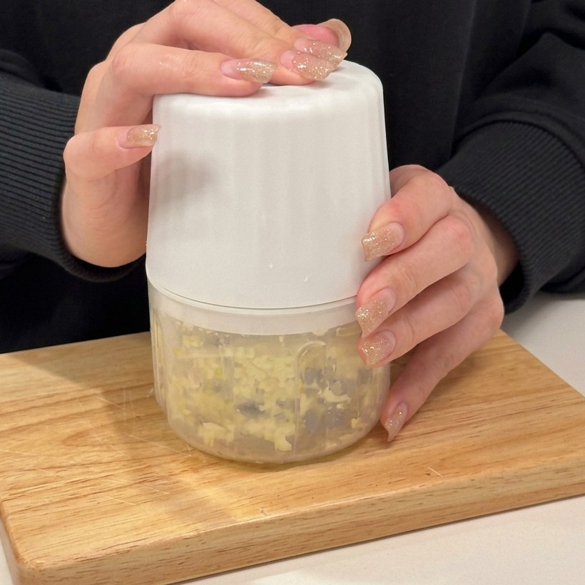 Minced garlic inside a small manual food processor on a wooden board.