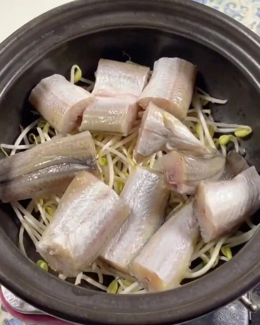 Pieces of fresh pollack neatly layered on top of bean sprouts in a dark clay pot.