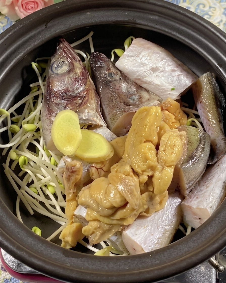 Fresh ginger slices and pollack roe placed over fish pieces in a pot.