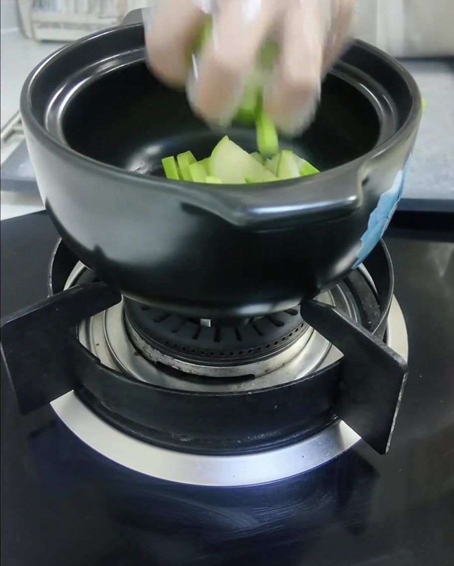 Raw sliced green squash and sliced white onions are placed into a black ceramic cooking pot.cite: 1