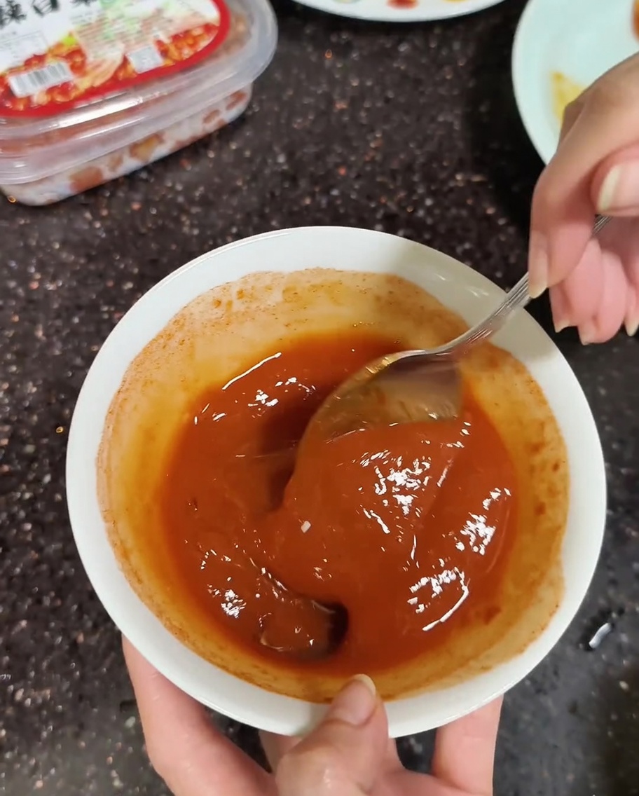 A close-up of a spoon mixing Korean soybean and chili pastes with a little water until smooth.