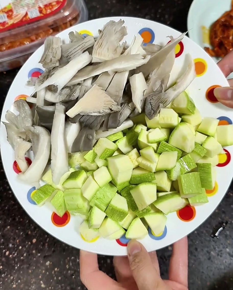 A plate holding fresh, sliced grey oyster mushrooms and diced light green zucchini ready for cooking.