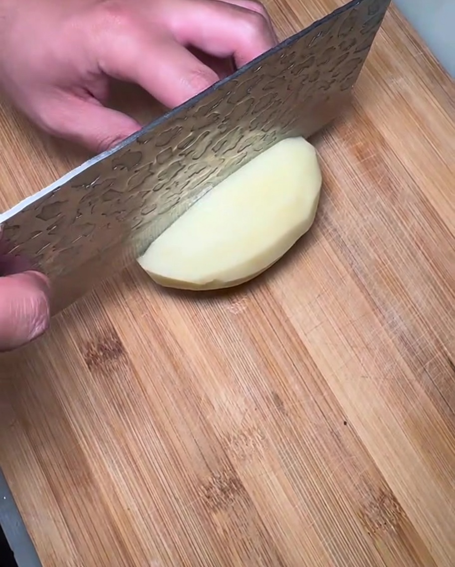 Slices of raw potato laid out on a wooden cutting board, ready for the stew.