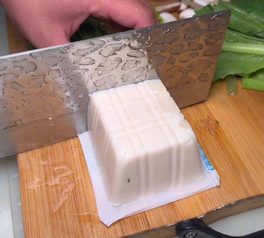 Soft silken tofu cut into thick blocks on a wooden cutting board.